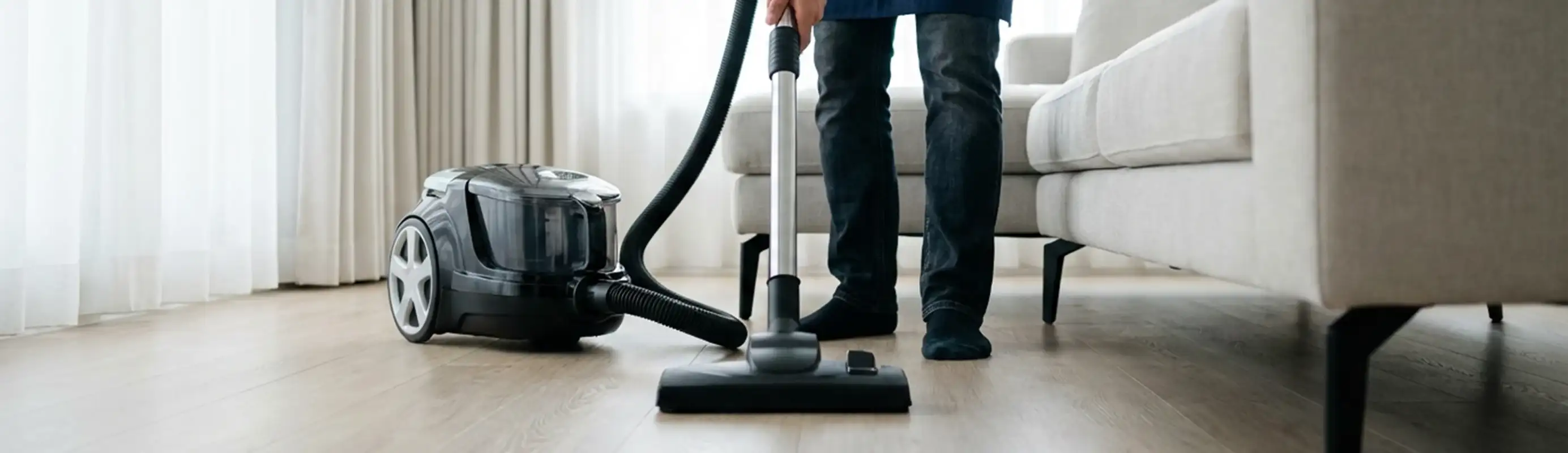 Professional house cleaner vacuuming a living room floor with a canister vacuum cleaner, Tampa, FL.