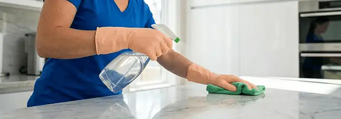 Maid service worker spraying and wiping a kitchen countertop with a microfiber cloth for sanitizing, Tampa, FL.