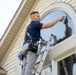 Professional window cleaner on a ladder using a squeegee to clean an exterior arched window, Tampa, FL.