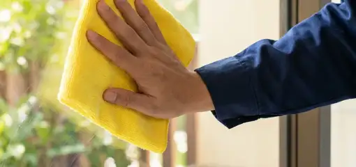 House cleaner wiping a glass window with a yellow microfiber cloth for streak-free cleaning, Tampa, FL.